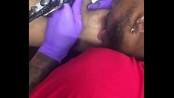 Horny tattoo artist multi-tasking sucking client's nipples